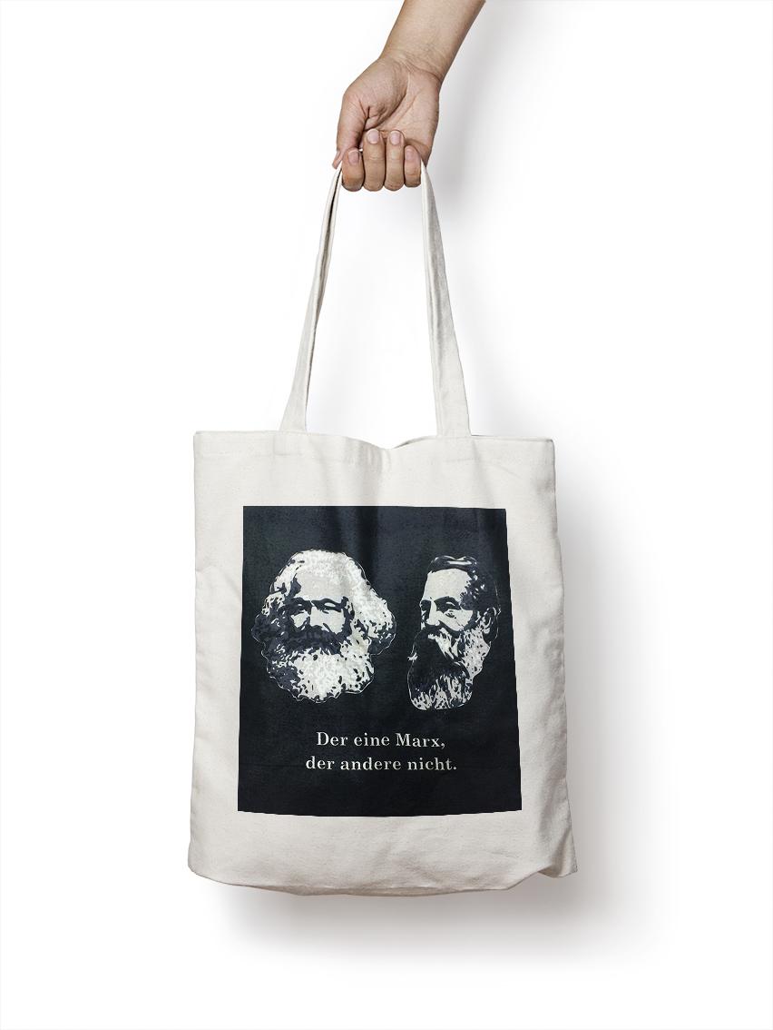 weiße Baumwolltasche mit gezeichnetem Kopf von Karl Marx und dem Spruch "Der eine Marx, der Andere nicht" auf schwarzem Quadrat weiße Baumwolltasche mit gezeichnetem Kopf von Karl Marx und dem Spruch "Der eine Marx, der Andere nicht" auf schwarzem Quadrat